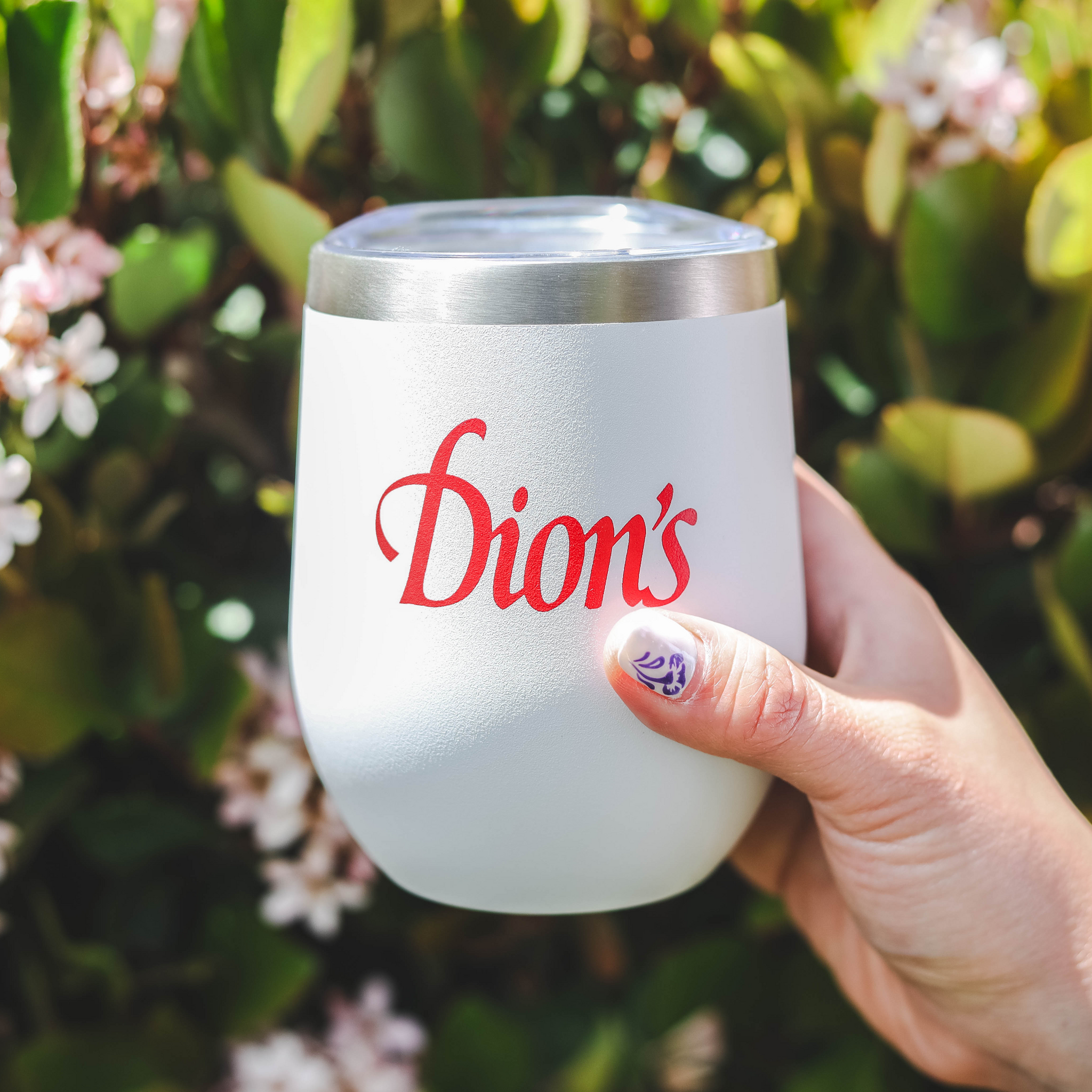 A hand holding a Dion's Fan Shop stainless steel tumbler with red text.