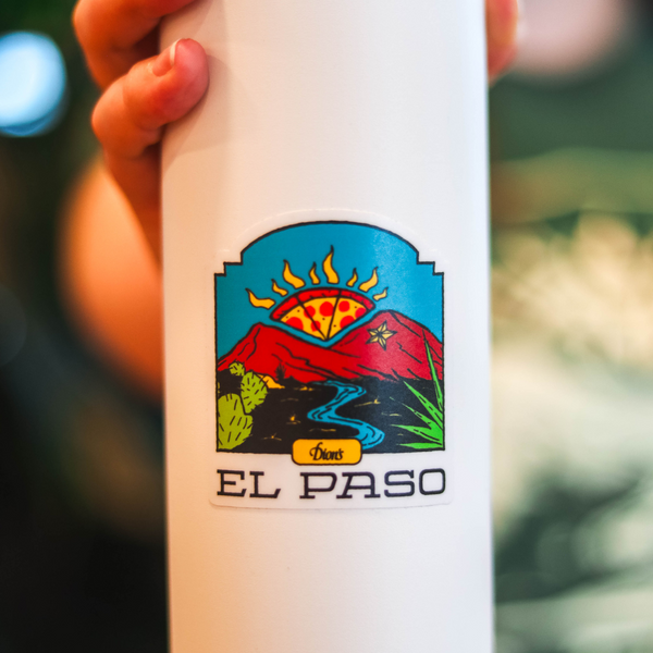 A person holds a white water bottle displaying a colorful El Paso Sticker by Dion's Fan Shop, featuring mountains, a river, a rising sun, and the text "El Paso," designed by Reyes Gonzalez.