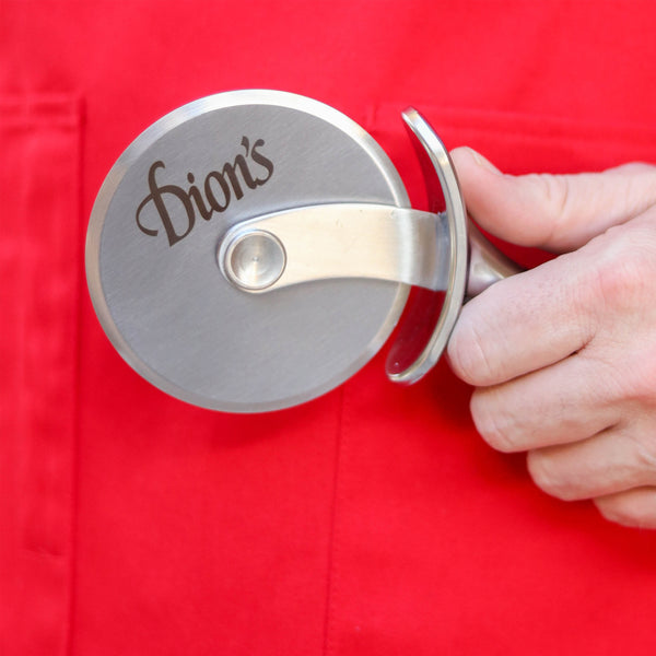 A person is holding a Dion's Fan Shop stainless steel red apron with a metal clip on it.
