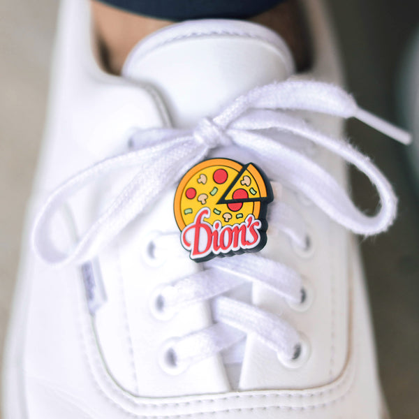 A pair of white footwear elevated by a Dion's Fan Shop Pizza Shoe Charm.