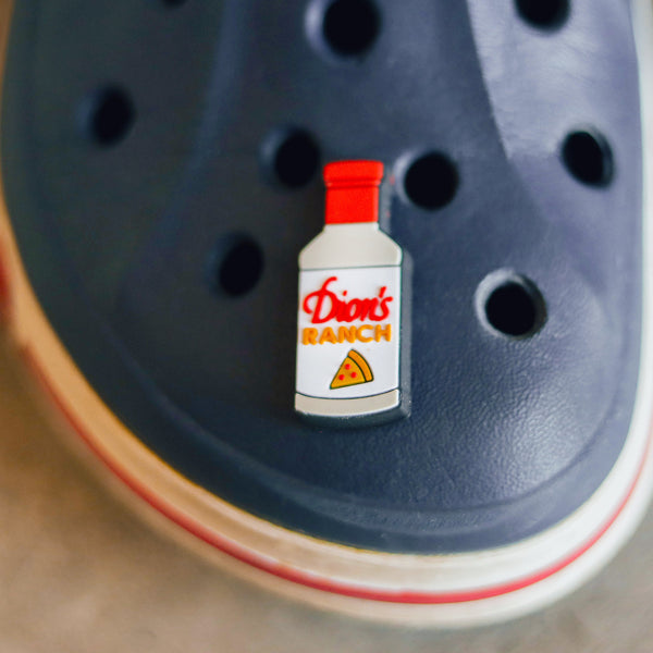 A Ranch Bottle Shoe Charm from Dion's Fan Shop sits on top of a pair of crocs.
