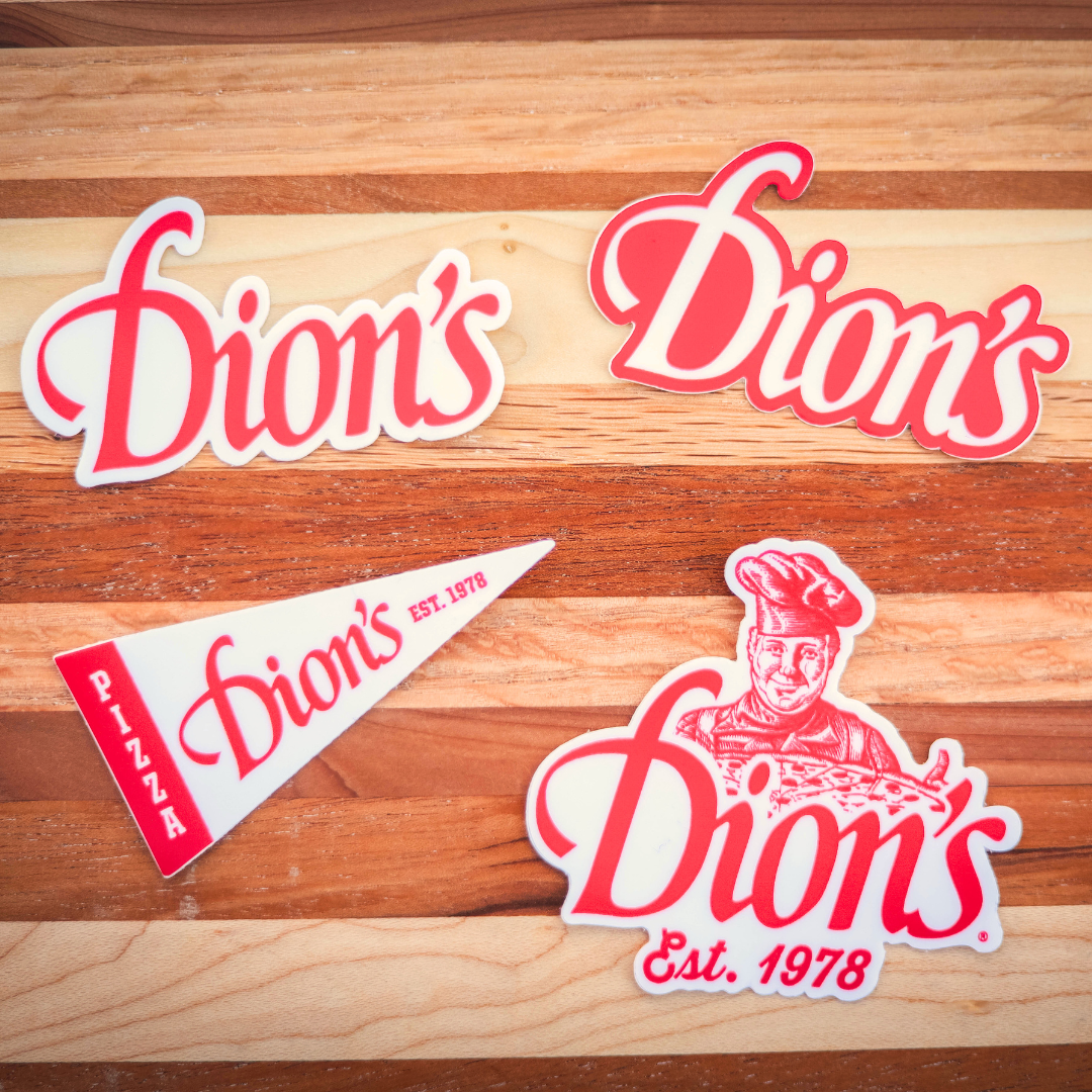 Red and white Dion's Ultimate Sticker Pack and a triangular paper with logo on a wooden surface.