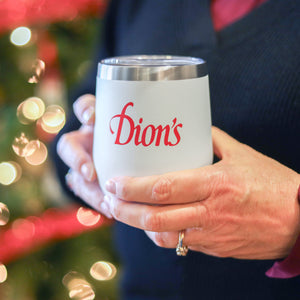 A woman holding a white wine tumbler with a red Dion's logo in front of a christmas tree.