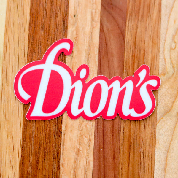 The Dion's Red Sticker from Dion's Fan Shop features the iconic logo on a wooden surface with striped light and dark wood—a stylish pizza decal for any fan.
