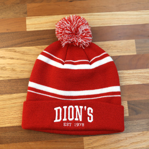 The Collegiate Beanie from Dion's Fan Shop features red and white stripes, a varsity pom-pom, and "DION'S EST. 1978" embroidered on the front, displayed on wood for a timeless, cozy vibe.