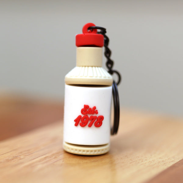 The Ranch Bottle Keychain from Dion’s Fan Shop features a bottle with "Est. 1978" in red on a white label, shown on wood—a playful tribute to Dion’s Ranch dressings.