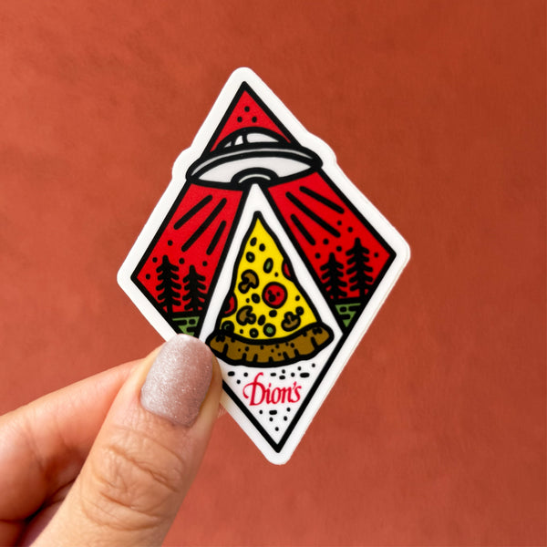 A hand holds the Roswell Dion's Sticker from Dion's Fan Shop, showing a UFO beaming up a pizza slice among trees with "Dion's" and "Roswell New Mexico" at the bottom.