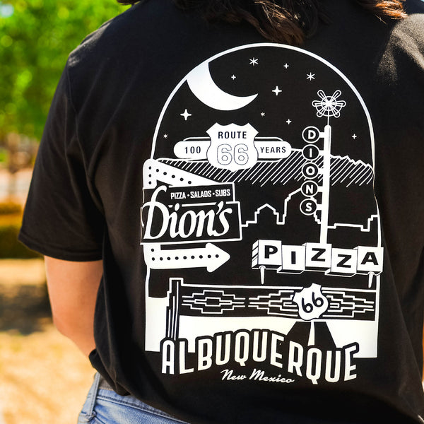 Someone wears a black Route 66 Centennial Tee from Dion's Fan Shop, featuring retro signage art and "Dion's Pizza", "Route 66 Centennial", and "Albuquerque, New Mexico" printed on the back.